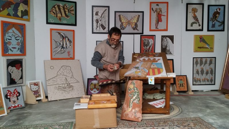 Barn, pictures, mosaic, man working. Table on carpet.