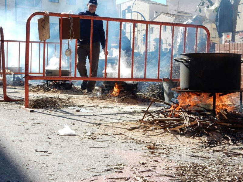 Strret, fire, wood, smoke, cooking pot. Man.