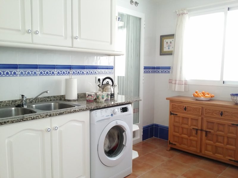 Kitchen, washing machine, sink, wooden sideboard, kettle, cups.